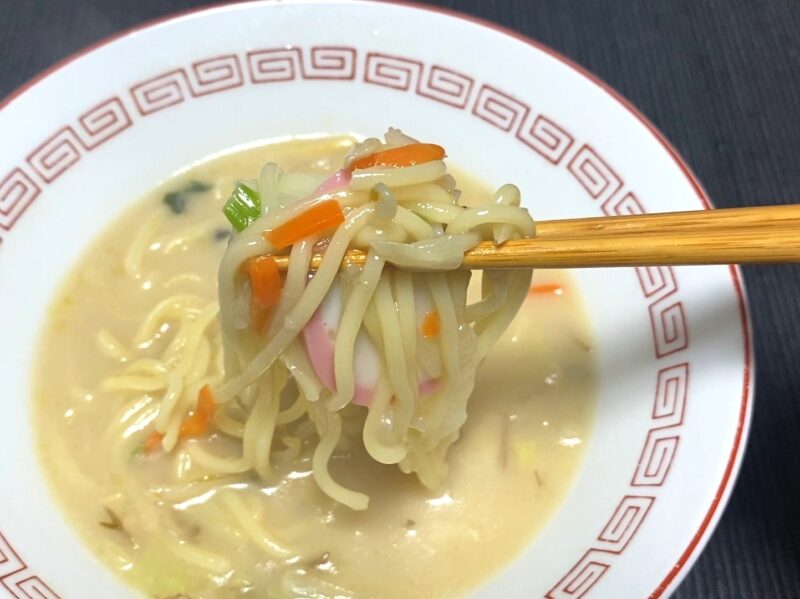 箸でつまんだちゃんぽんの具材アップ。もやし・にんじん・かまぼこが白濁スープに絡まっている