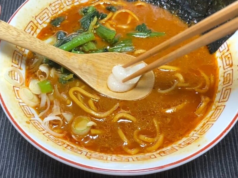 山岡家乾麺・辛味噌にニンニクをレンゲで投入する様子・赤いスープとほうれん草・ネギ