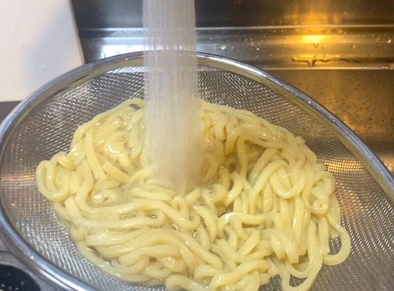 加熱後の麺をザルに移し、流水で冷やして締める調理工程