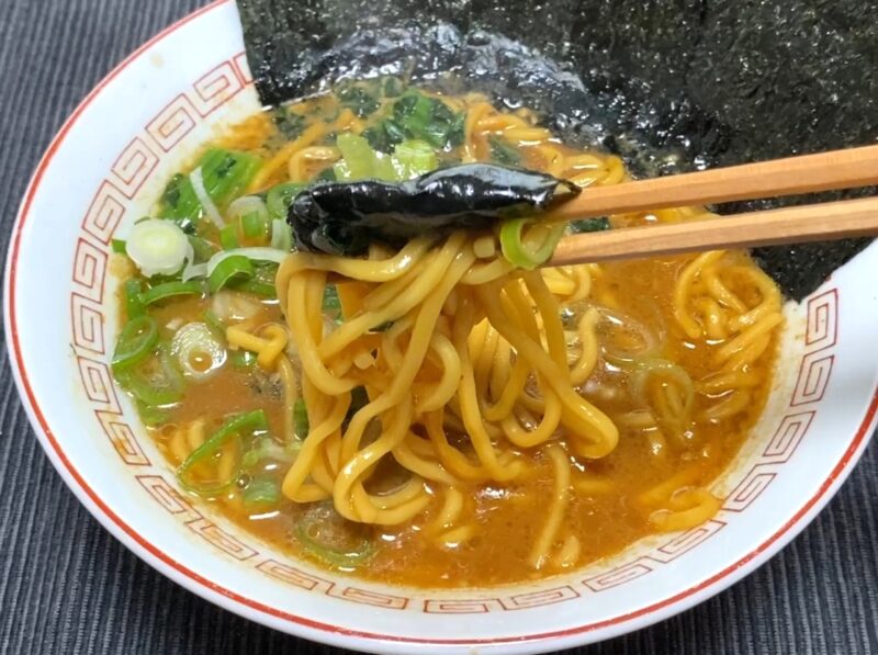 山岡家乾麺・特製味噌に海苔・ほうれん草・ネギをトッピングして箸で麺と海苔を持ち上げた様子