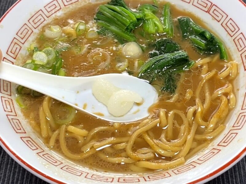 山岡家乾麺・醤油にニンニクを乗せたレンゲをスープに入れる様子