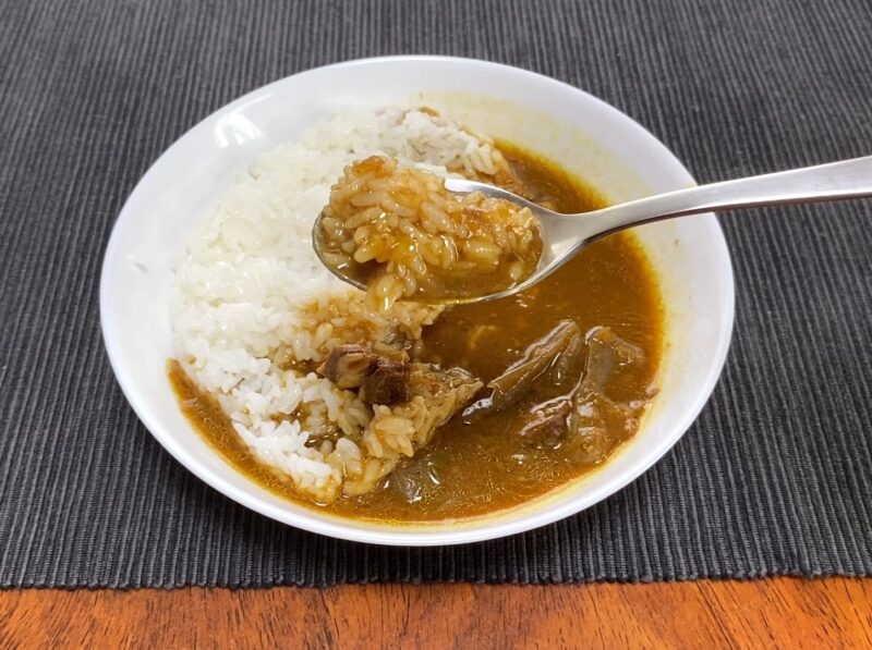 業務スーパー・牛すじとこんにゃくの和風カレーのルーがご飯に染み込んだ様子・ビチャビチャになったご飯をスプーンですくう