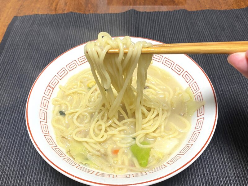 箸で持ち上げたお水がいらないちゃんぽんの中太麺。白濁スープとキャベツが見える