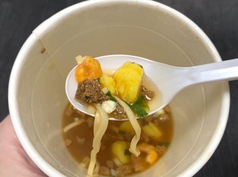 コスモスON365・旨口しょうゆヌードルの具材アップ・エビ・卵・そぼろ・豚肉・ネギをレンゲにのせた様子