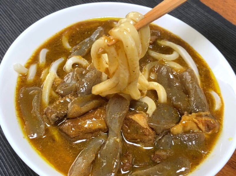 業務スーパー・牛すじとこんにゃくの和風カレーうどんを箸で持ち上げた様子・和風カレーが絡んだコシの強いうどん