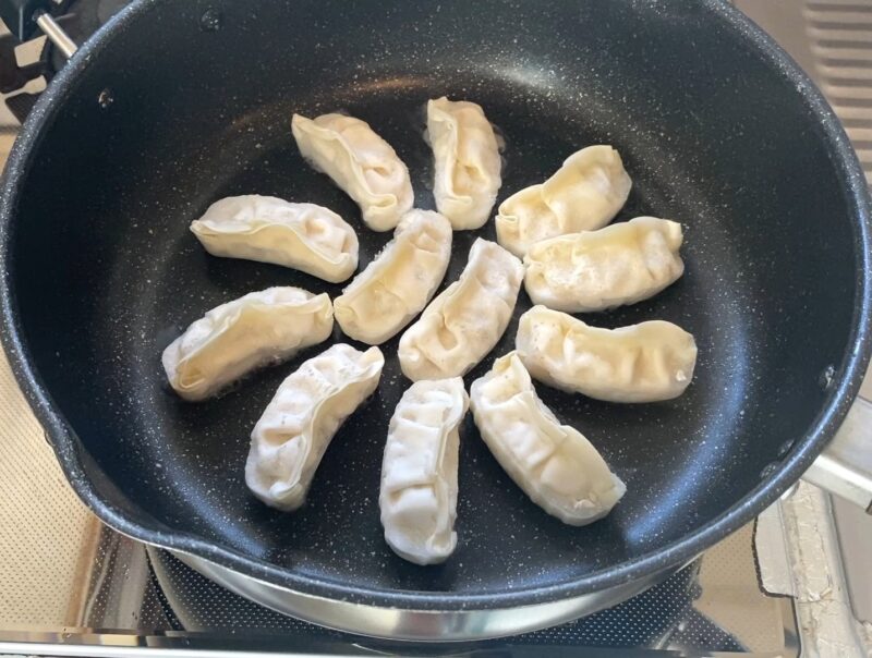 コスモス羽根つきギョーザをフライパンに並べて加熱中の様子。凍ったまま中火で焼いている