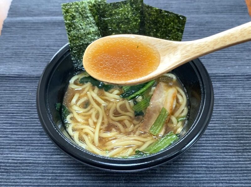 木製レンゲで吉村家ラーメンの豚骨醤油スープをすくったアップ。澄んだ茶色のスープに油が浮く様子