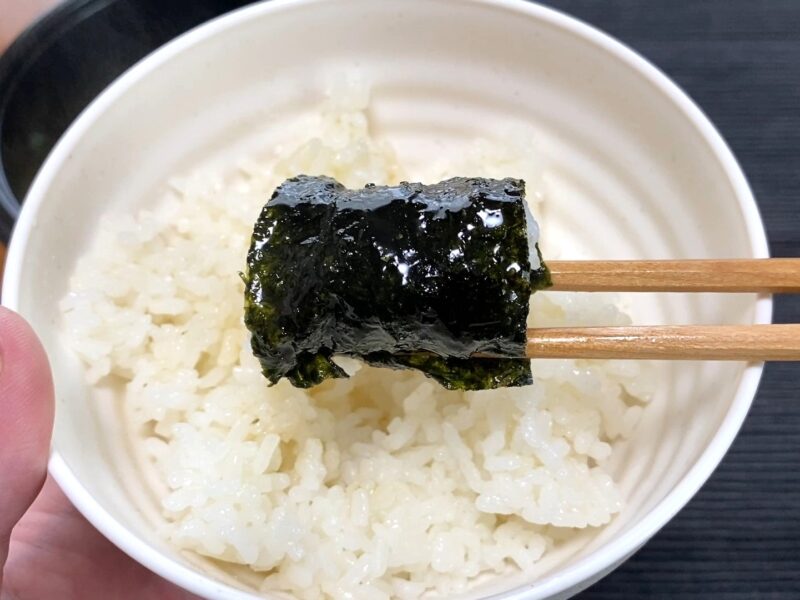 スープを吸った焼き海苔をご飯の上に乗せて箸で持ち上げたアップ。家系ラーメンの海苔ご飯アレンジ