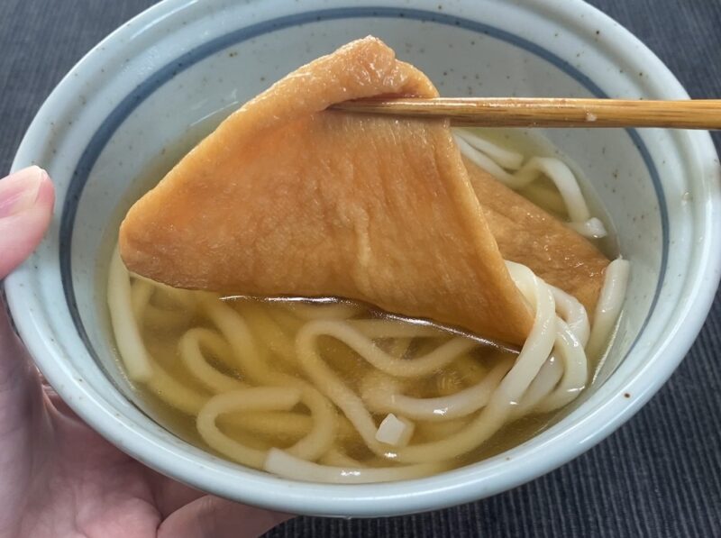 箸で大判おあげを持ち上げたアップ。甘じょっぱくふっくら仕上がった油揚げの質感