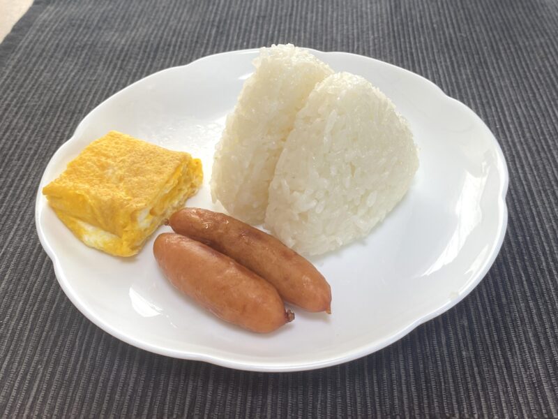 電子レンジ調理後の塩むすび2個を卵焼き・ウインナーと一緒に白い皿に盛り付けた実食の様子