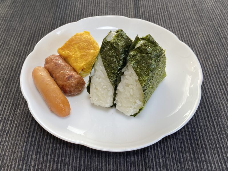 海苔を巻いた塩むすび2個を卵焼き・ウインナーと一緒に白い皿に盛り付けた様子
