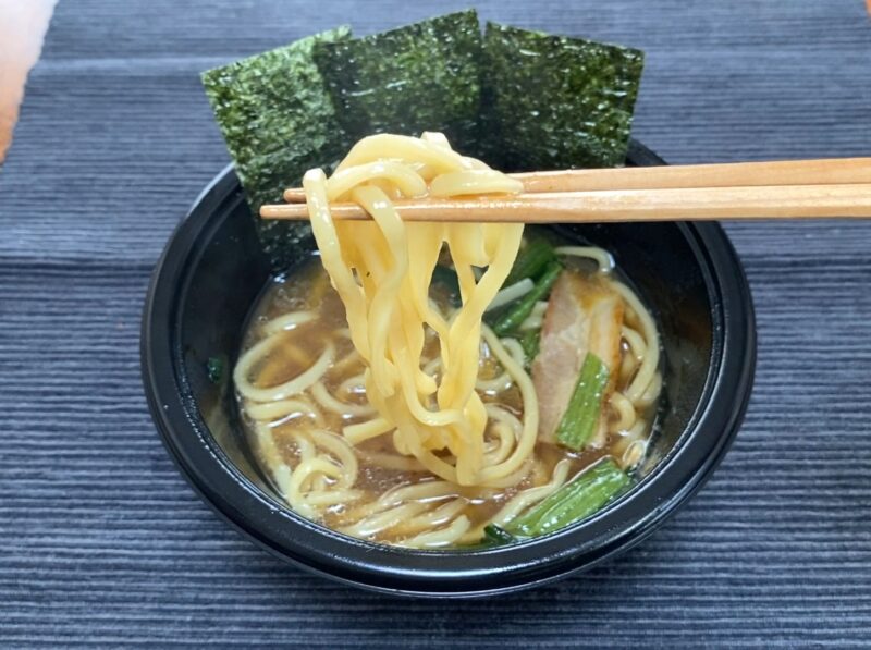 箸で吉村家ラーメンの中太もっちり麺を持ち上げたアップ。スープが絡んだ麺の質感がわかる