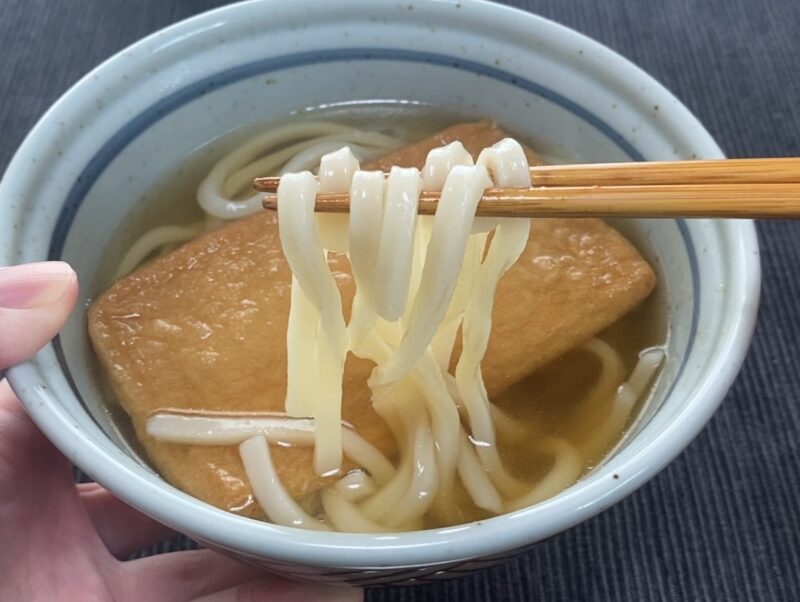 箸で讃岐きつねうどんの麺を持ち上げたアップ。コシのあるツルツルとした讃岐うどんの麺