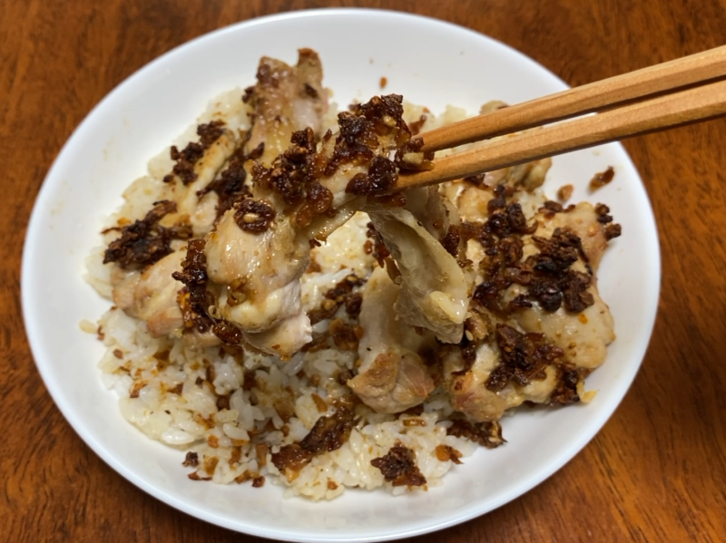 焼き上がった鶏もも肉をご飯に乗せ、箸で持ち上げたところ。表面に焦げたガーリックチップが付いている