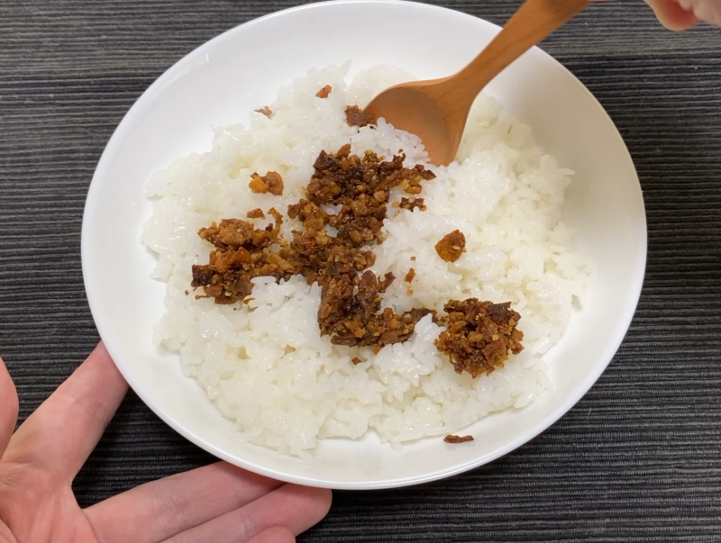 白いご飯にガーリックライスの素を乗せ、木のスプーンで混ぜ始めたところ。素が固まりのまま残っている
