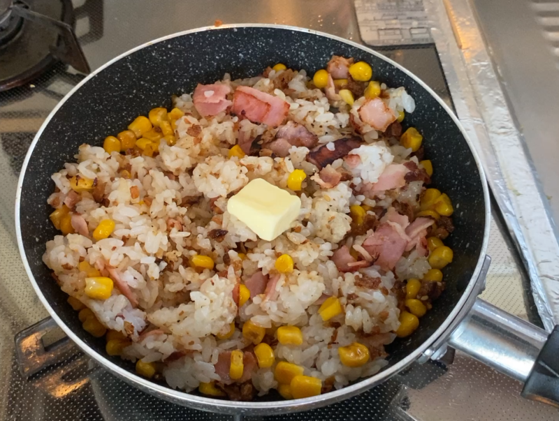 フライパンで炒めたベーコンとコーン入りのガーリックライス。中央にバターが乗っている